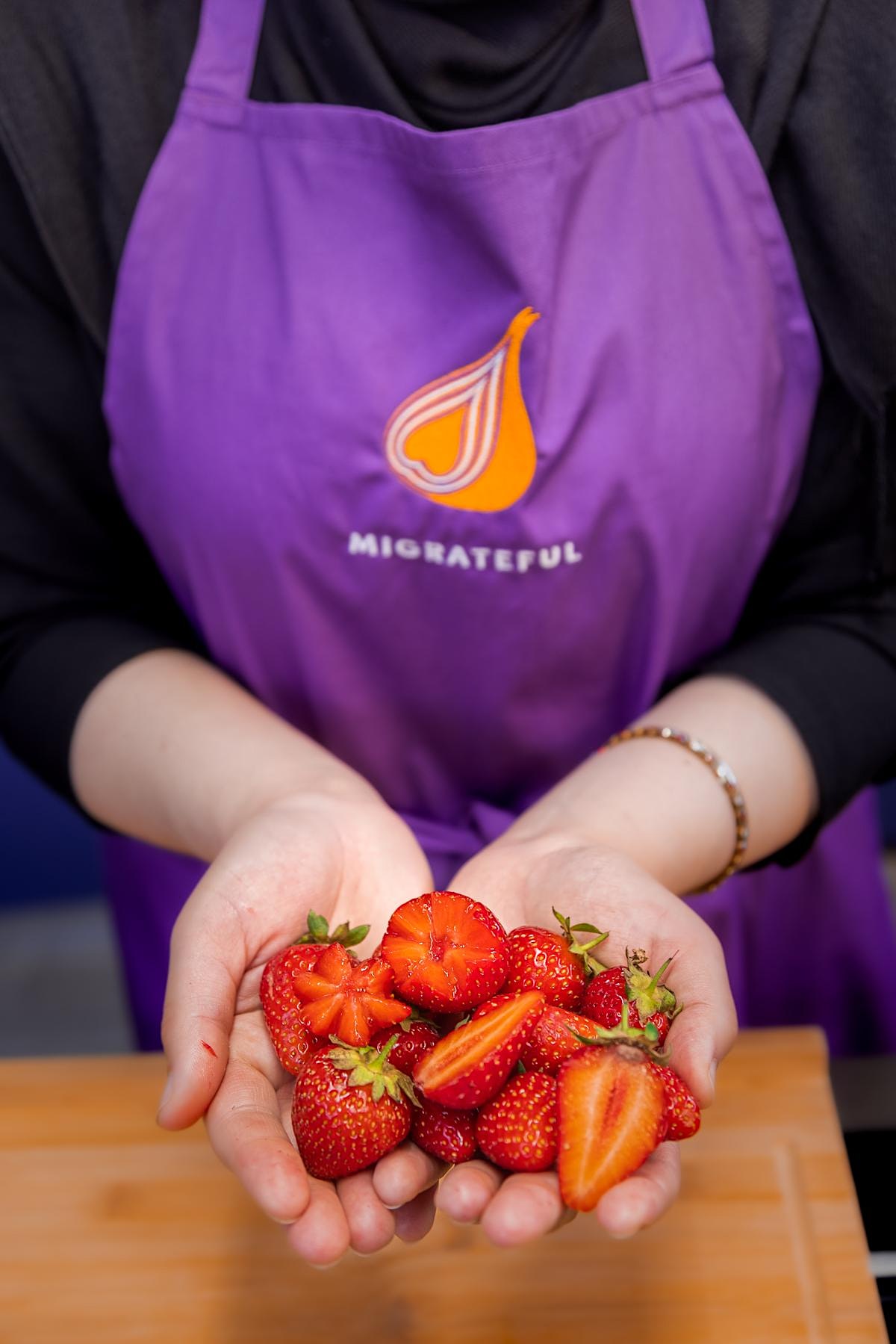 A woman in a purple apron holding strawberries participating in a London Cookery Class with Migrateful.