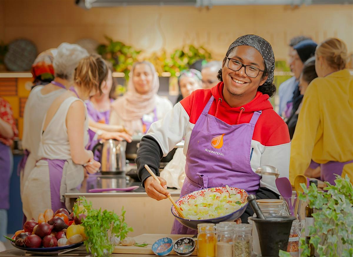 A Migrateful cook in a purple apron smiling during a London Cookery Class.