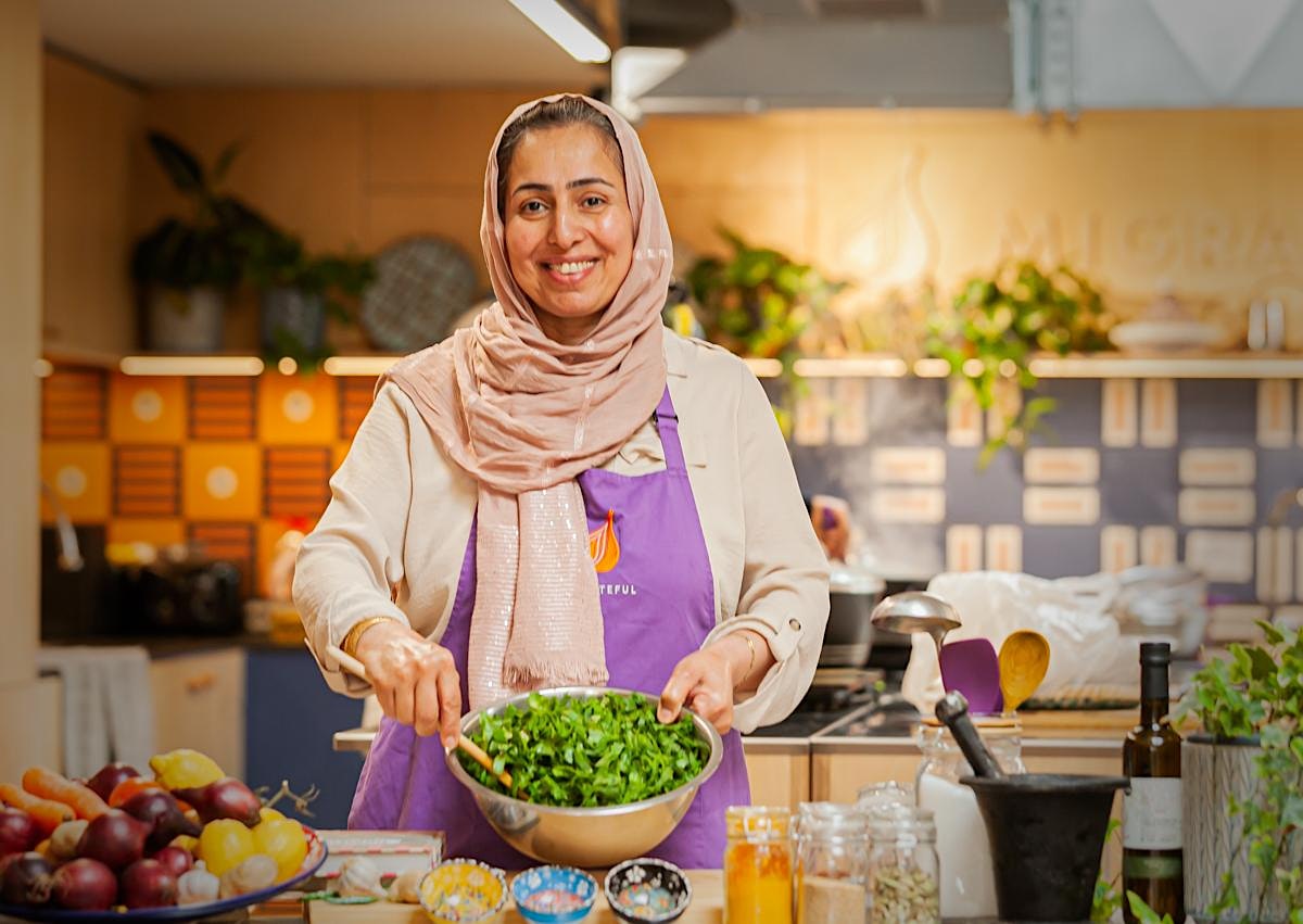 A Migrateful participant in an apron is preparing food in a London Cookery Class kitchen.