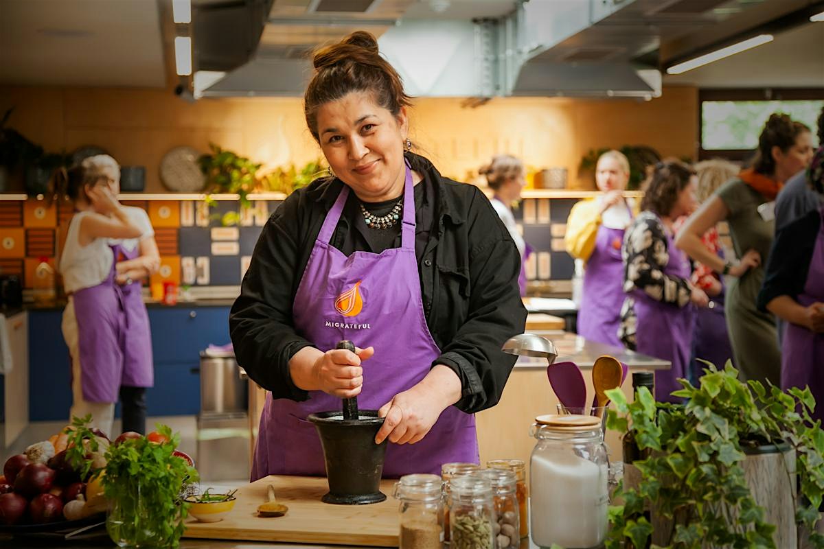 A Migrateful London Cookery Class instructor, donning a purple apron, skillfully prepares food in a kitchen.
