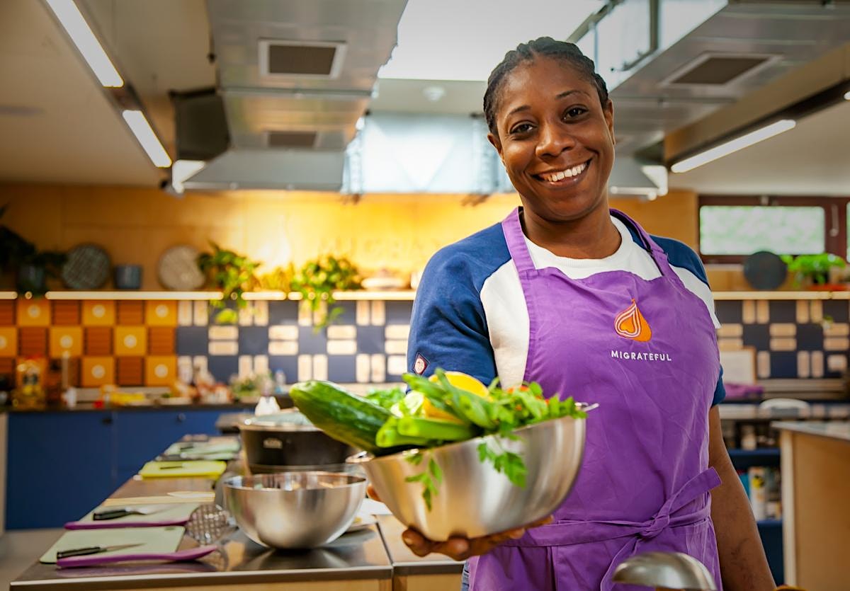A woman in a purple apron, from Migrateful's London Cookery Class, holding a bowl of vegetables.