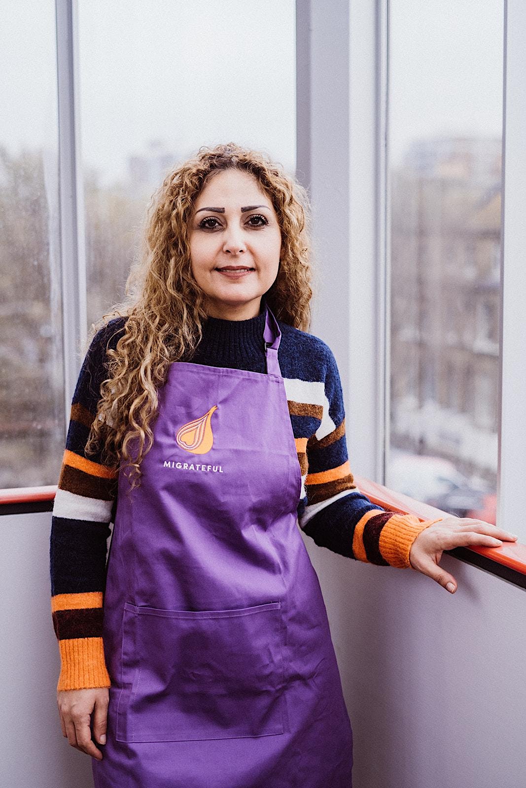 A woman in a purple apron standing in front of a window during a London Cookery Class.