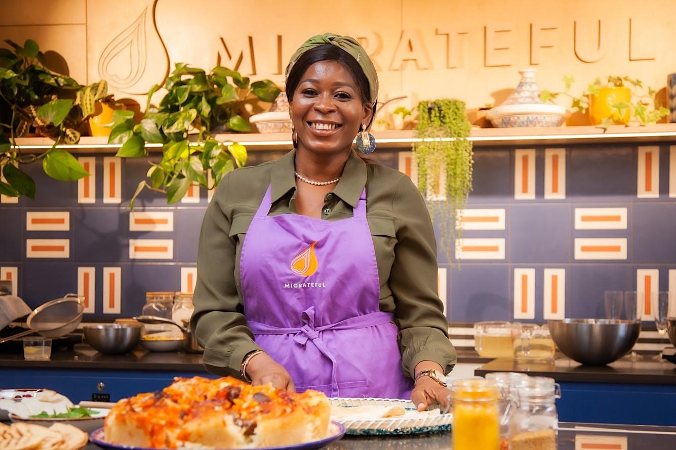 A woman in an apron standing in front of delicious and beautifully prepared food at a London Cookery Class by Migrateful.