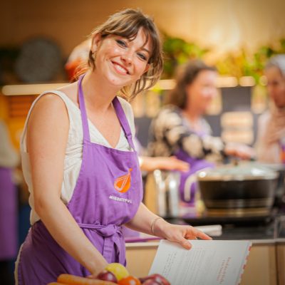 Thea Sands wearing a purple Migrateful apron in the Migrateful Cookery School